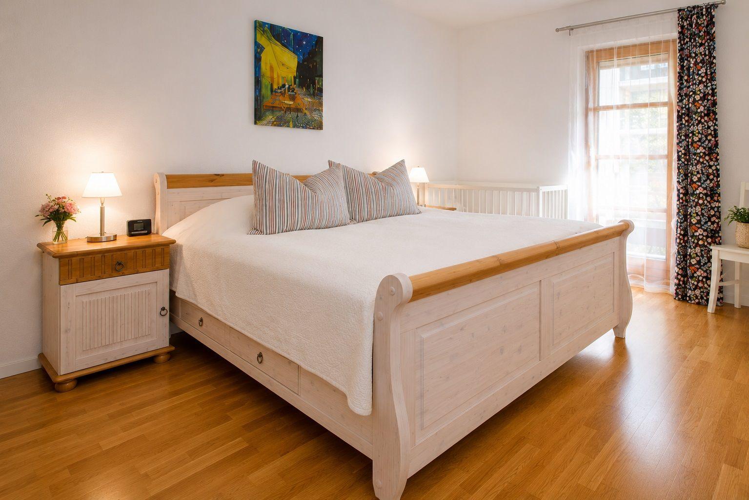 Schlafzimmer mit Bett, Nachttisch und Fenster mit Vorhängen.