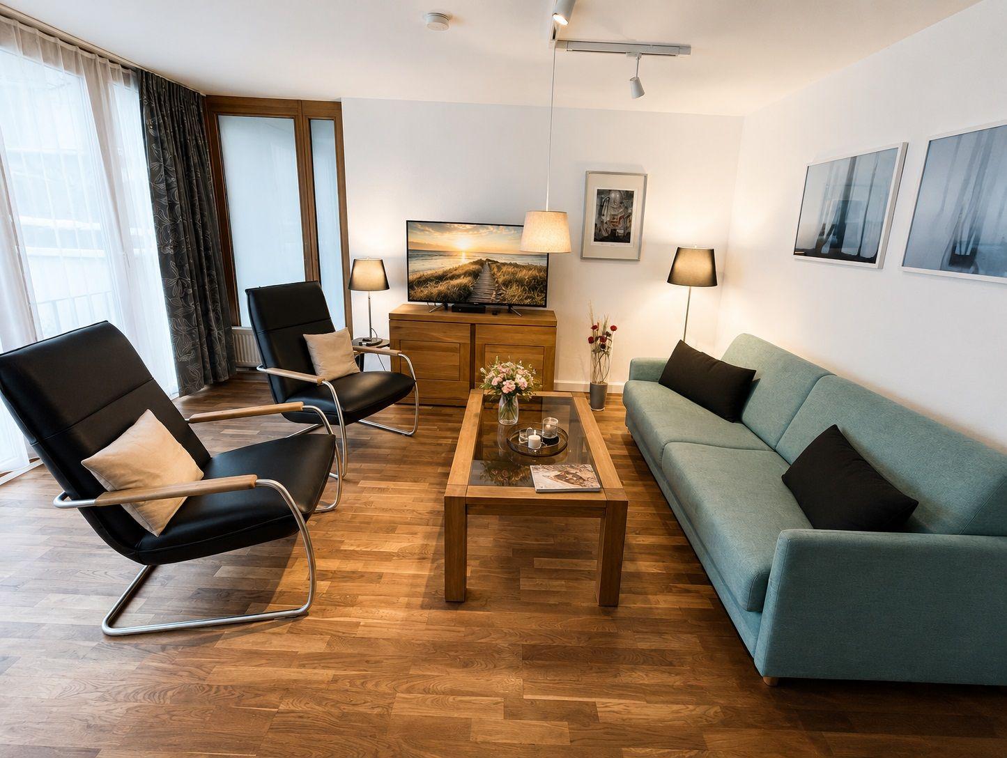 Ein Wohnzimmer mit Sofa, zwei Sesseln, Fernseher und Holzboden.