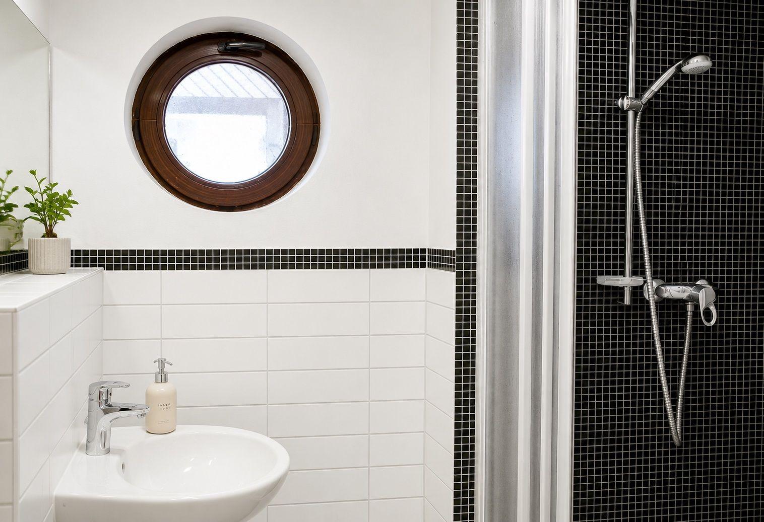 Badezimmer mit runden Fenster, Waschbecken und Dusche mit Mosaikfliesen.
