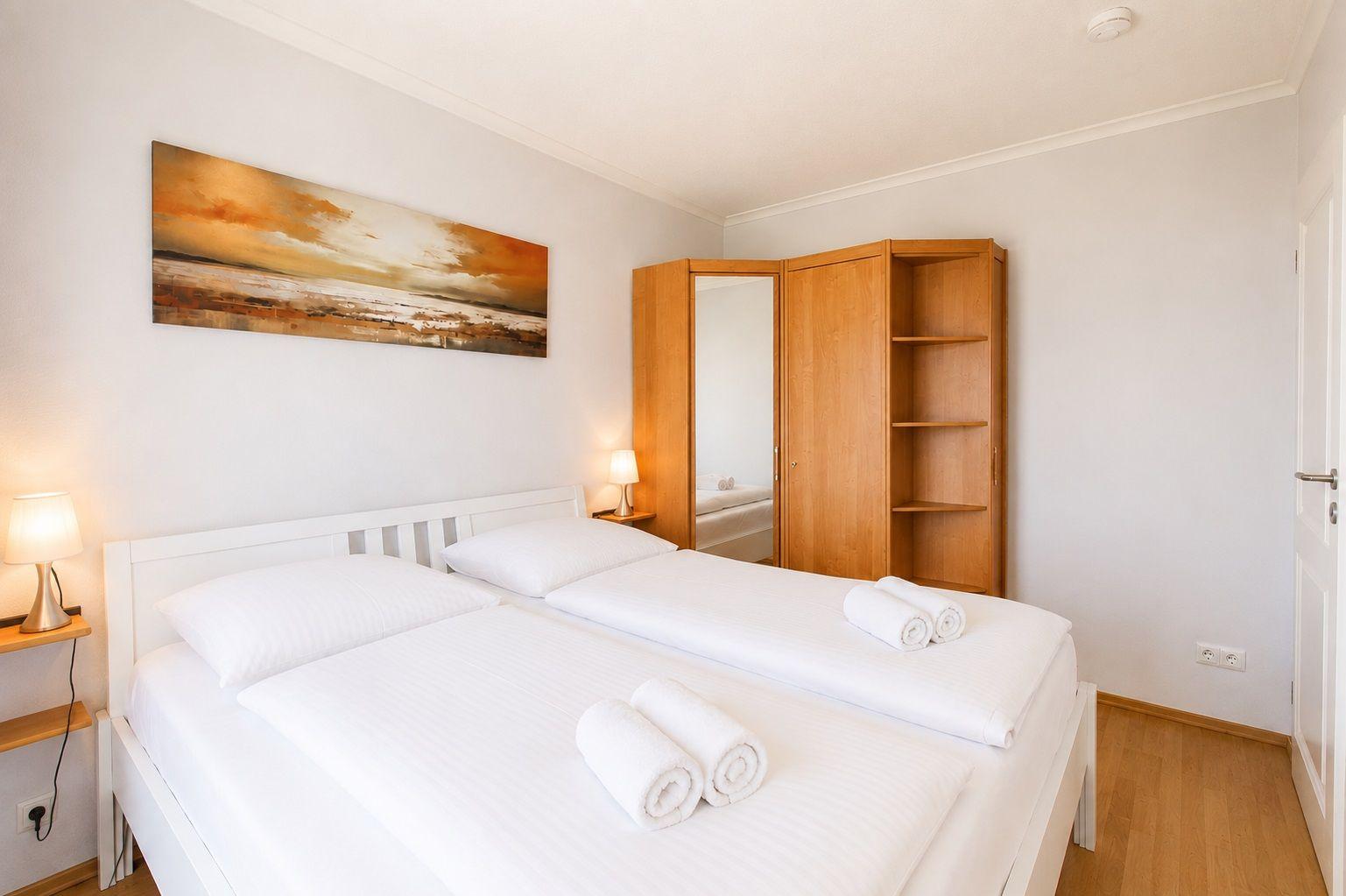 Schlafzimmer mit Doppelbett, Holzschrank und Wandbild.