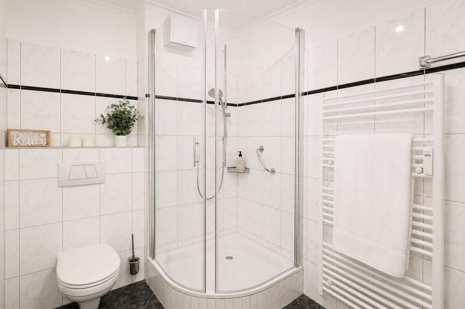 Badezimmer mit Dusche, Toilette und Heiztrockner. Weiße Fliesen und schwarze Akzente.