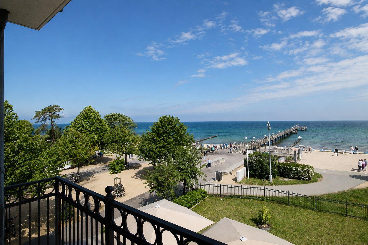 Blick vom Balkon auf Strand, Pier und See unter blauem Himmel mit weißen Wolken.