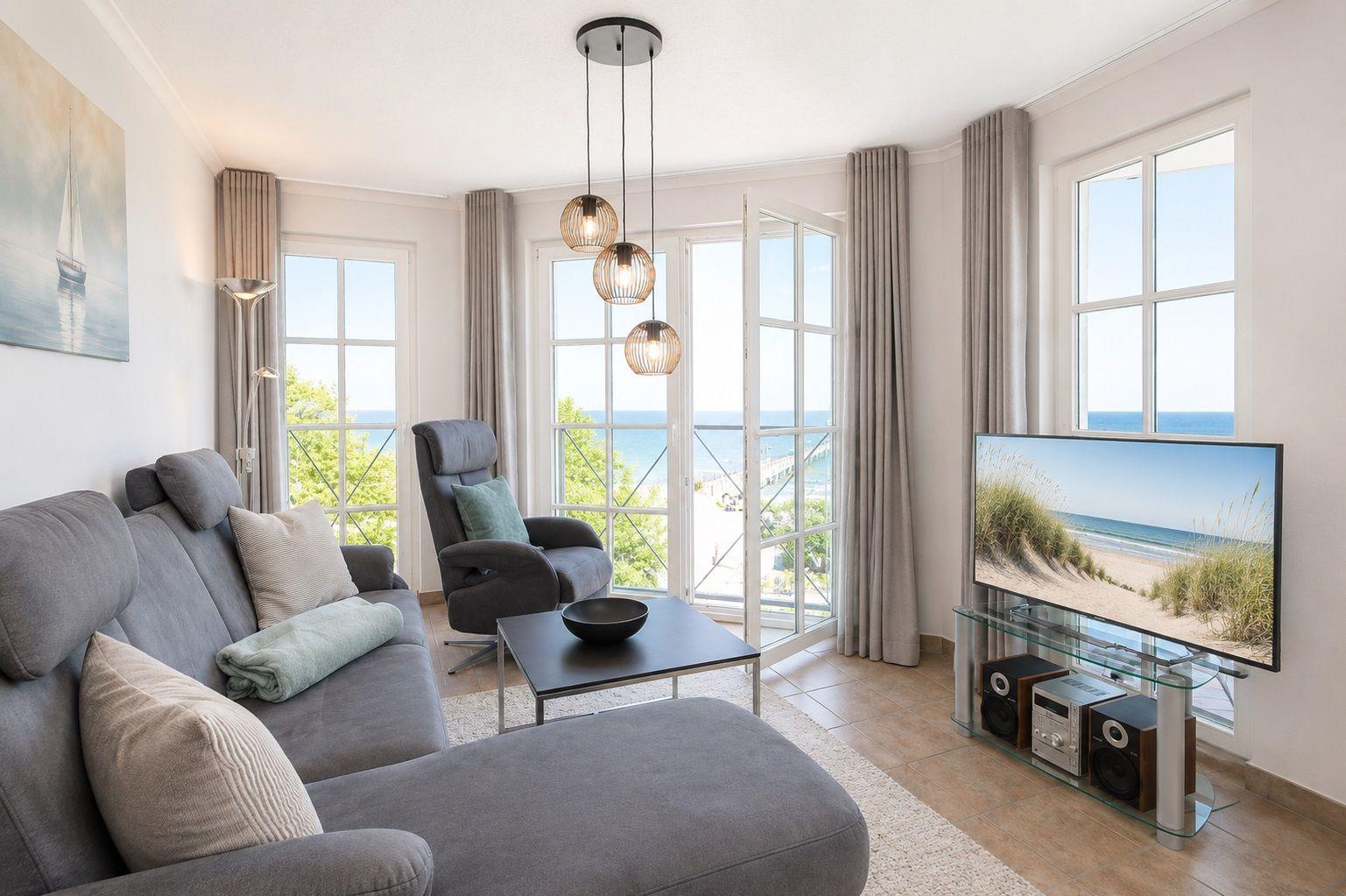 Essbereich mit Blick auf das Meer und Balkon. Wohnbereich mit Sofa und TV.