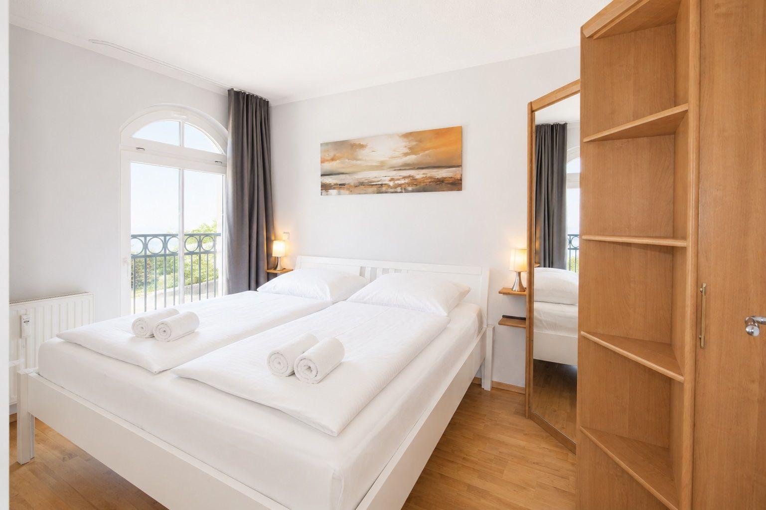 Schlafzimmer mit Doppelbett, Balkon und Holzschrank.