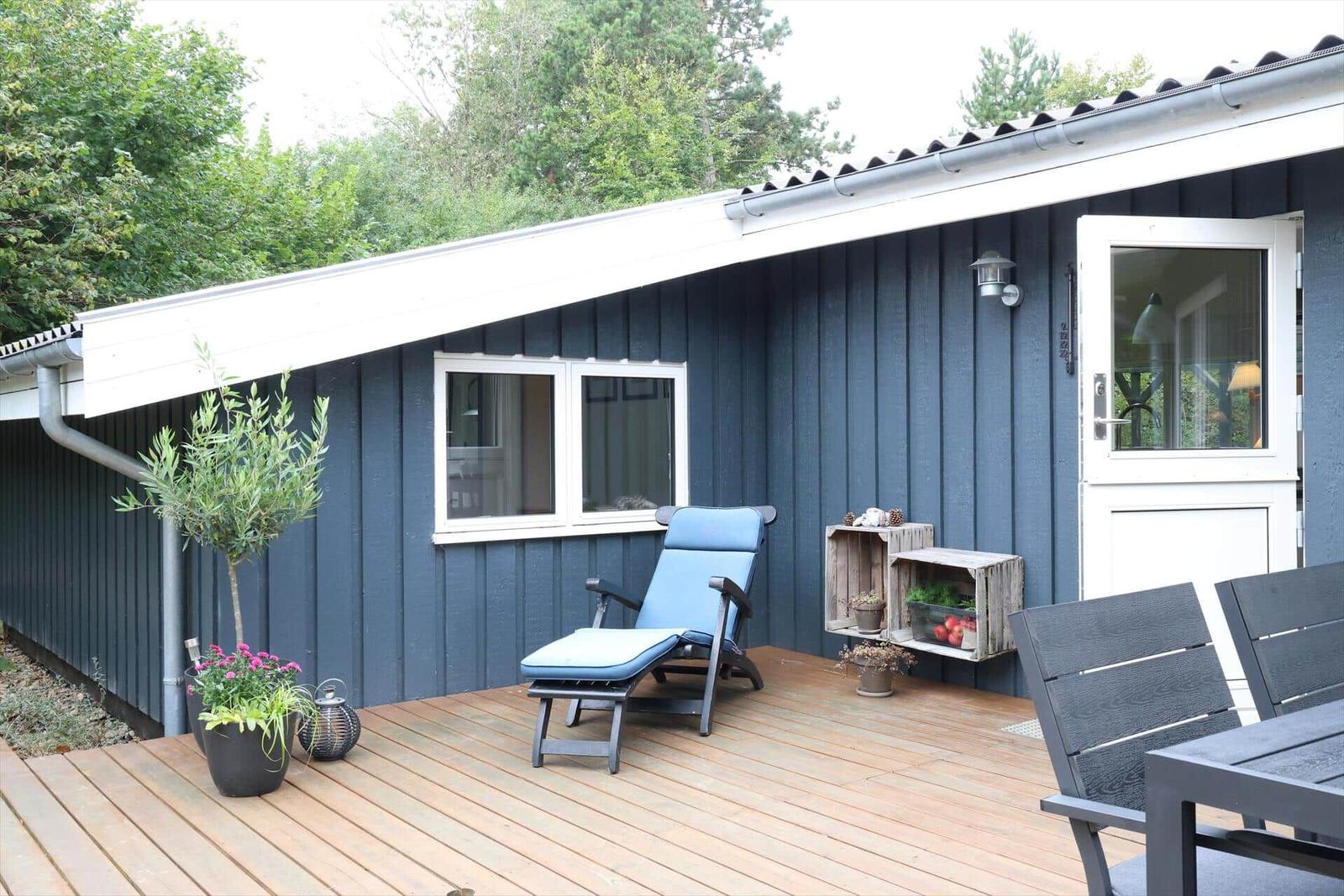 Deck with table, two chairs, and plants in baskets. Dark blue wood wall and glass door.