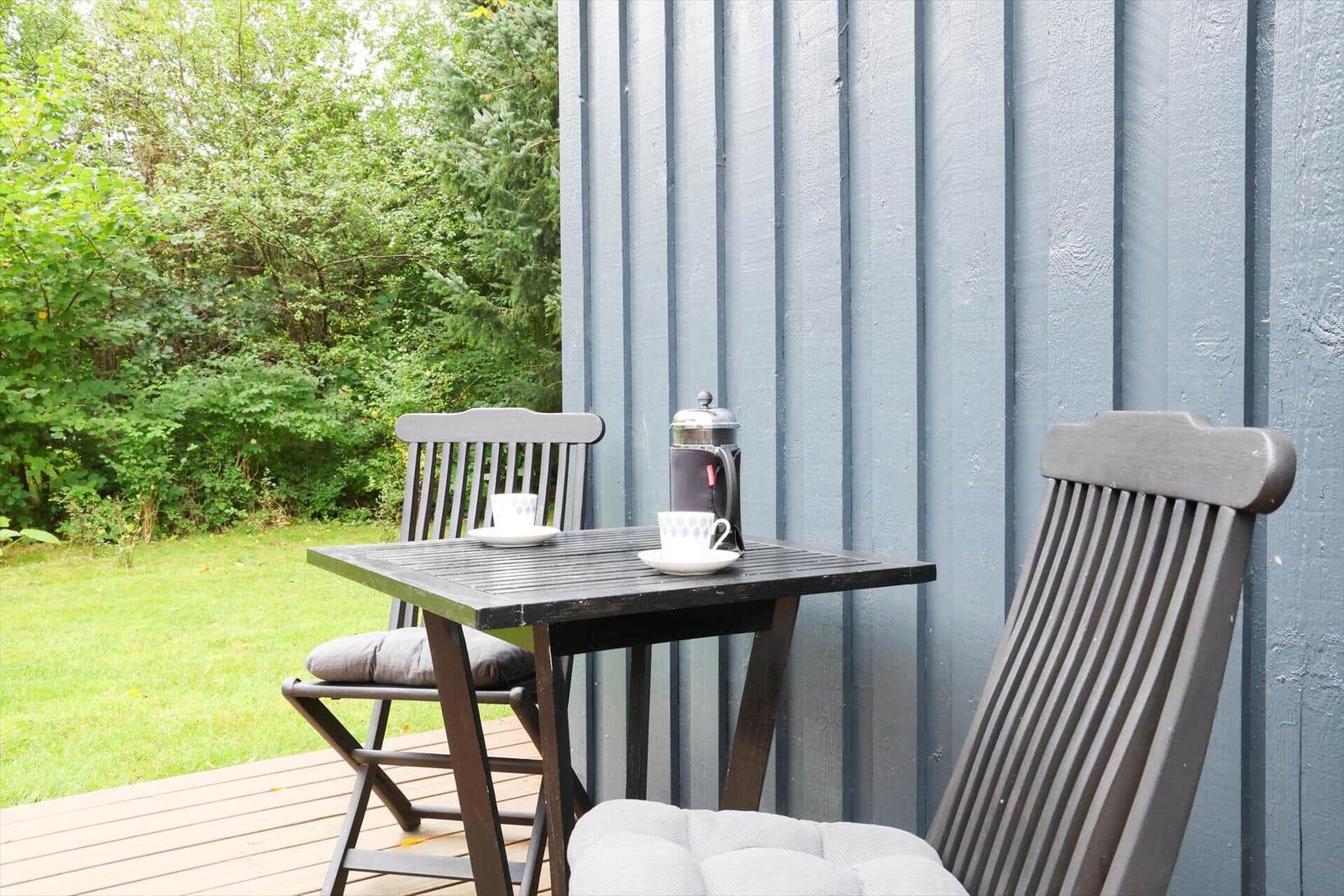 Round table with chairs on terrace, surrounded by greenery and sunflowers.