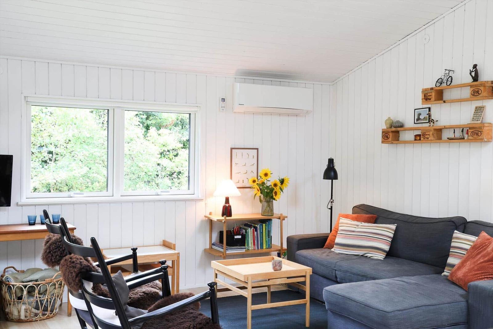 Two single beds with pillows and blankets stand under a window with a view of greenery.