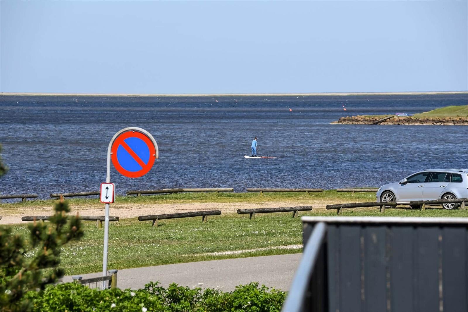 Segelboard liegt auf Gras, im Hintergrund Wassersportler auf dem See.