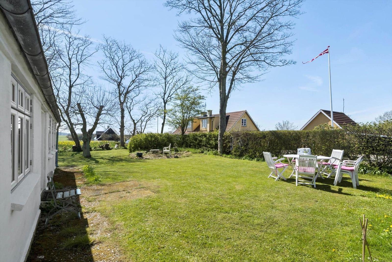 Haus mit Garten, Tisch und Stühlen im Freien. Blick auf das weiße Gebäude mit dunklem Dach.