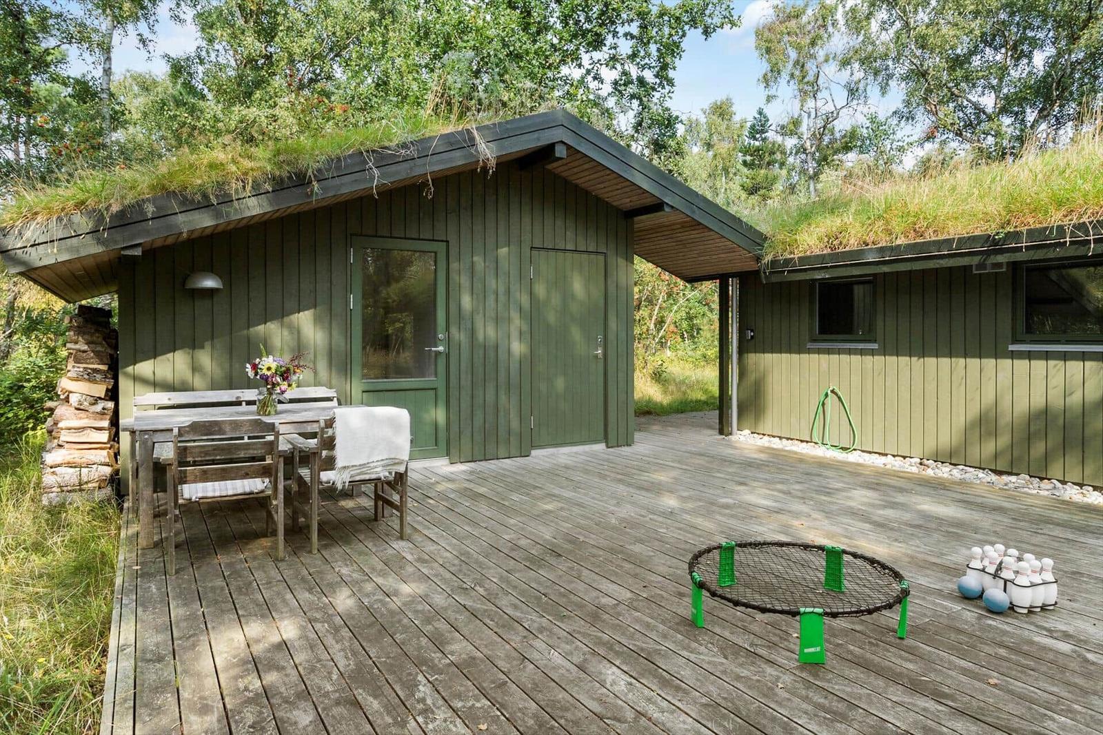 Holzterrasse mit Tisch, Stühlen und Liegestühlen vor einem Haus mit Grasdach.