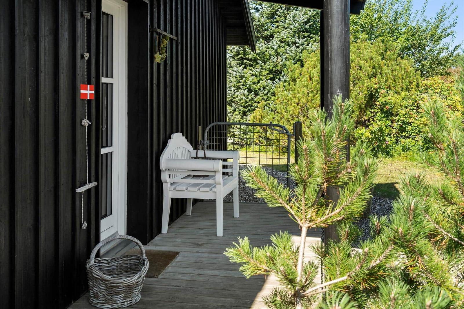 Terrasse mit weißem Tisch und Stühlen, Holzdecke und Grill. Tür führt ins Haus.