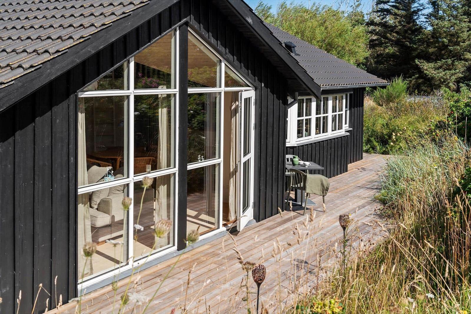Schwarze Holzhütte mit weißem Fenster und grünem Metallbank auf Holzterrasse.