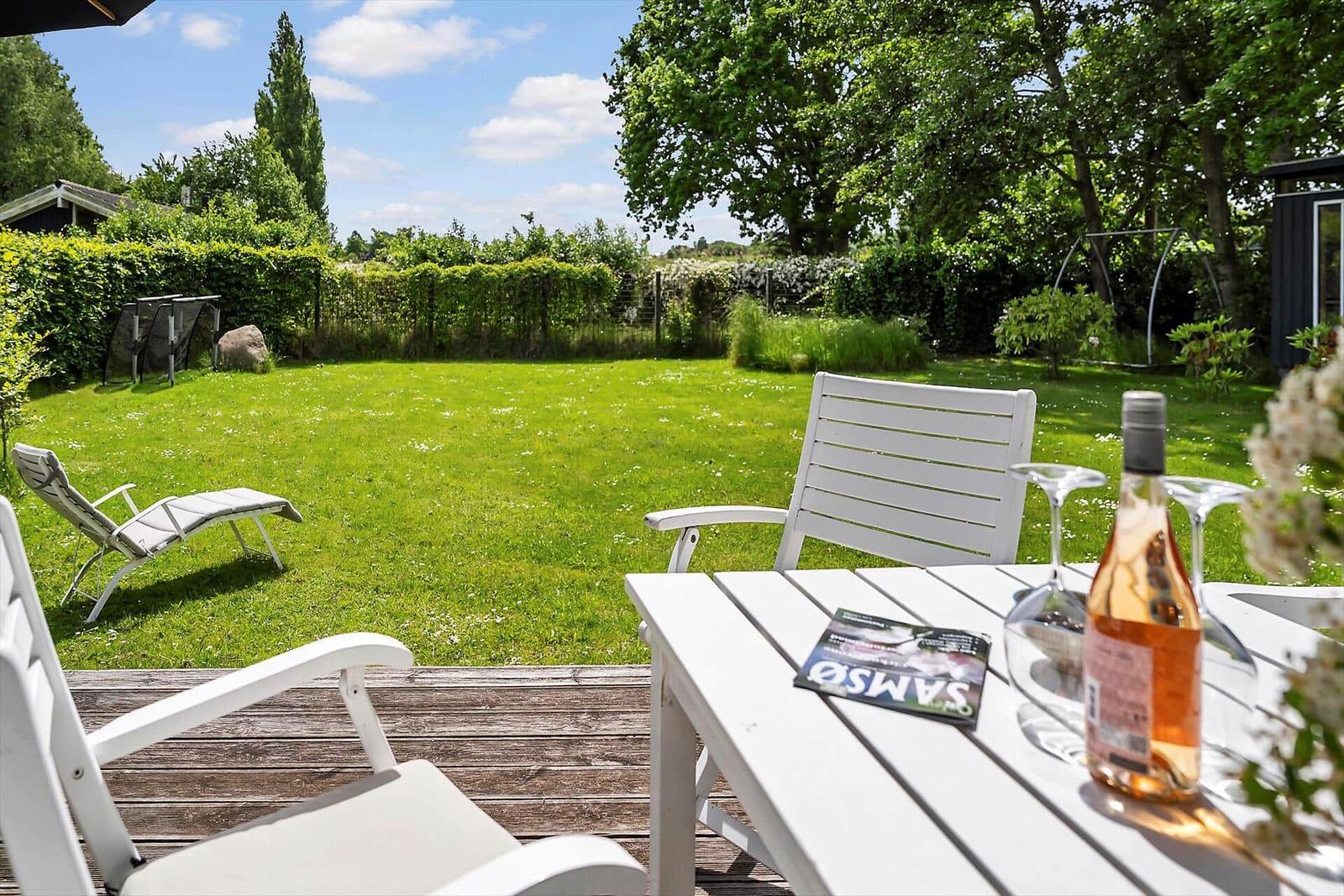 Terrasse mit weißem Tisch und Stühlen, umgeben von Grün und einem Garten.