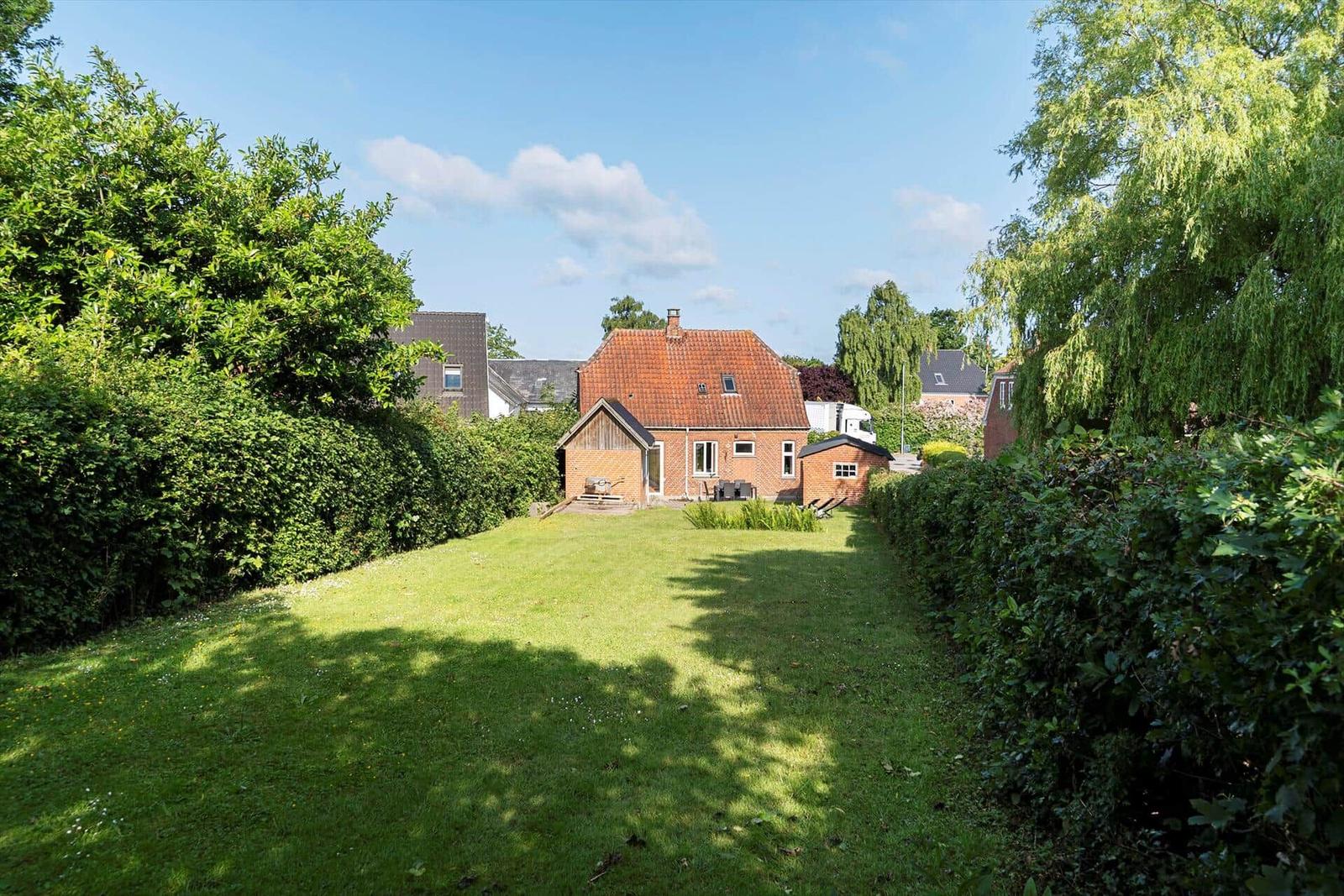 Red brick house with garden and terrace with table and chairs.
