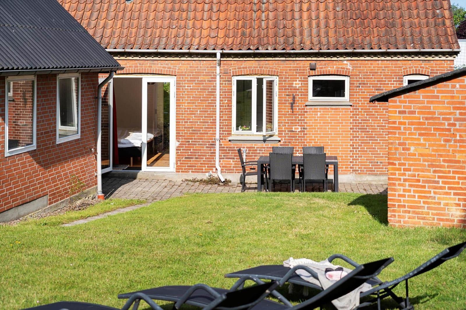 Red tiled roof, patio with table and chairs, garden and trees in the background.