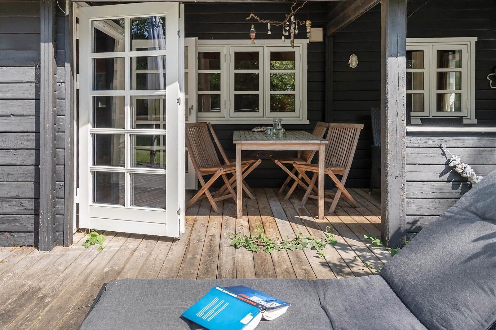 Porch with wooden table, chairs, and windows overlooking greenery.