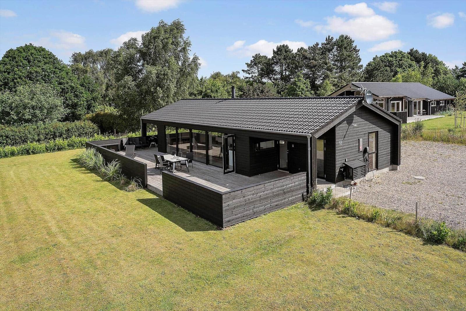 Modern black wooden cabin with terrace and garden in rural setting.