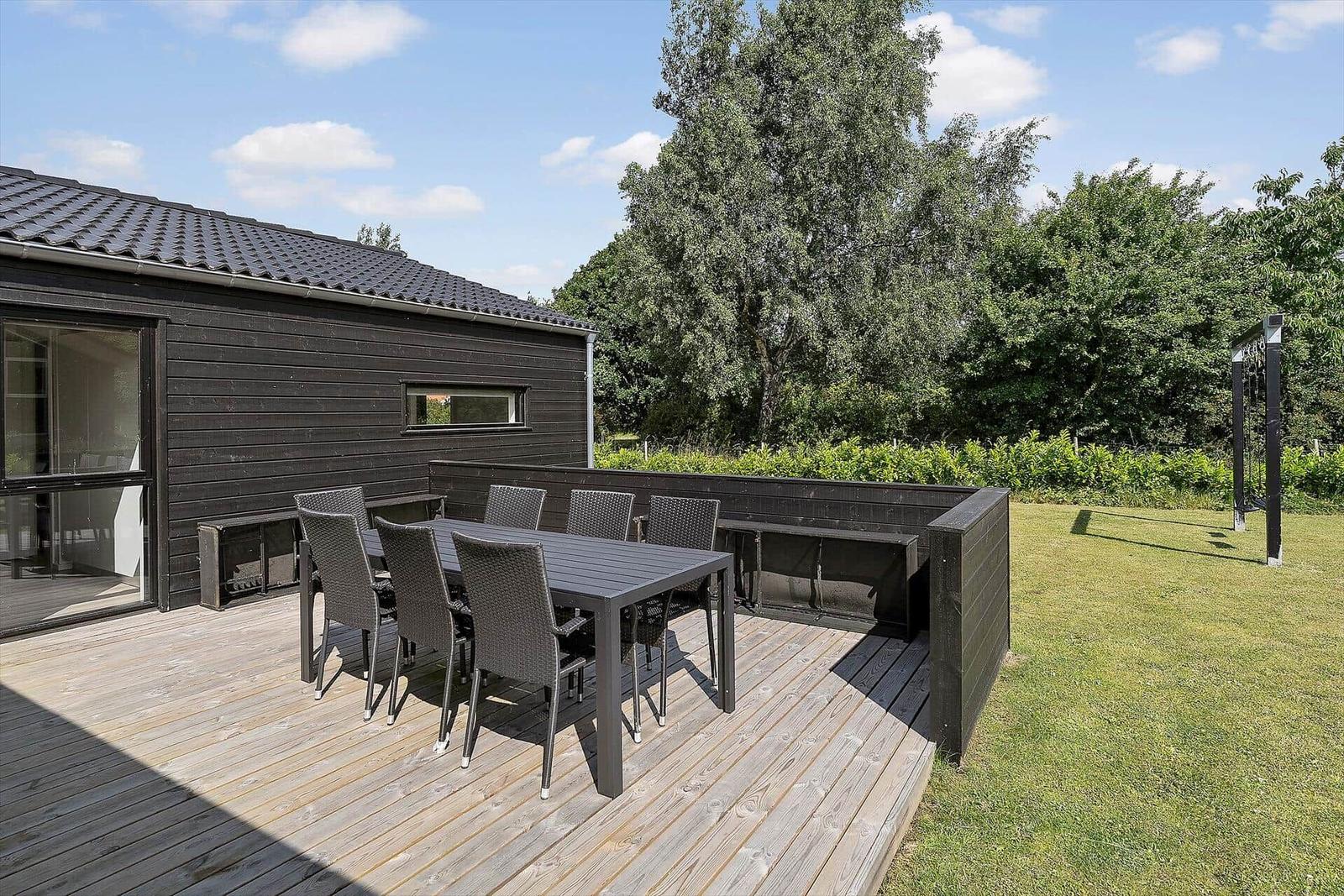 Deck with lounge chair, table, and chairs. Large glass facade to interior.