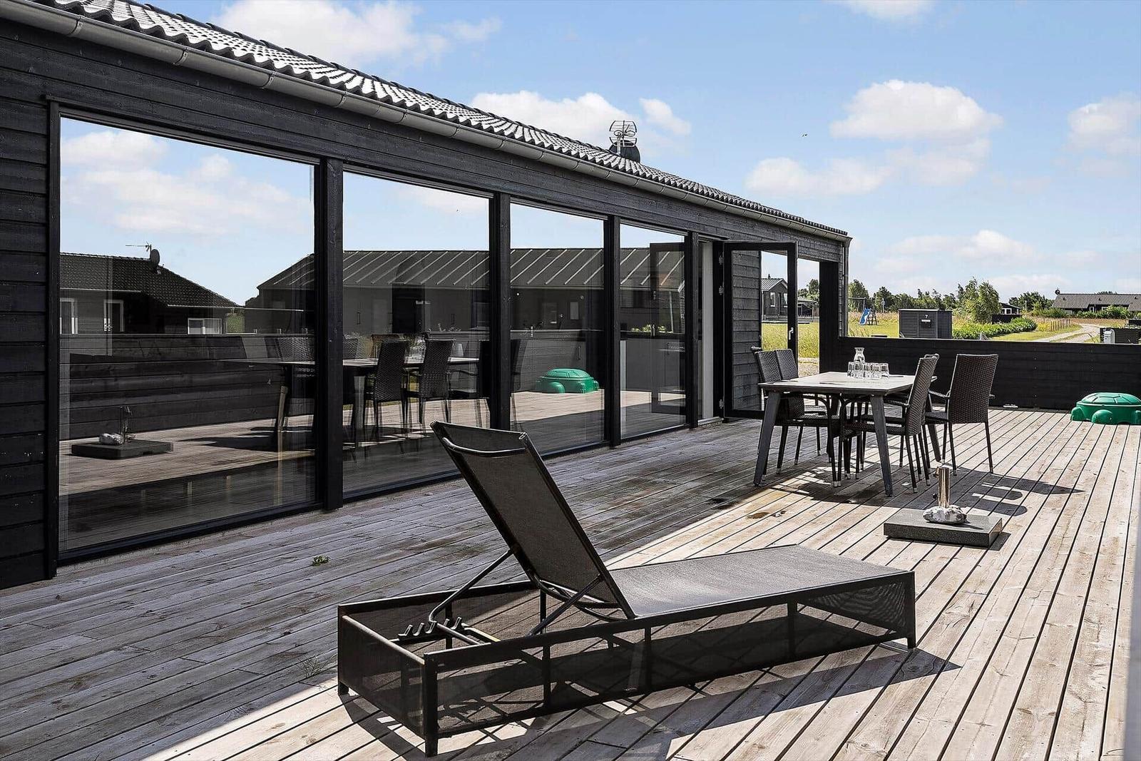 Deck with table and chairs, surrounded by trees and a wooden wall.