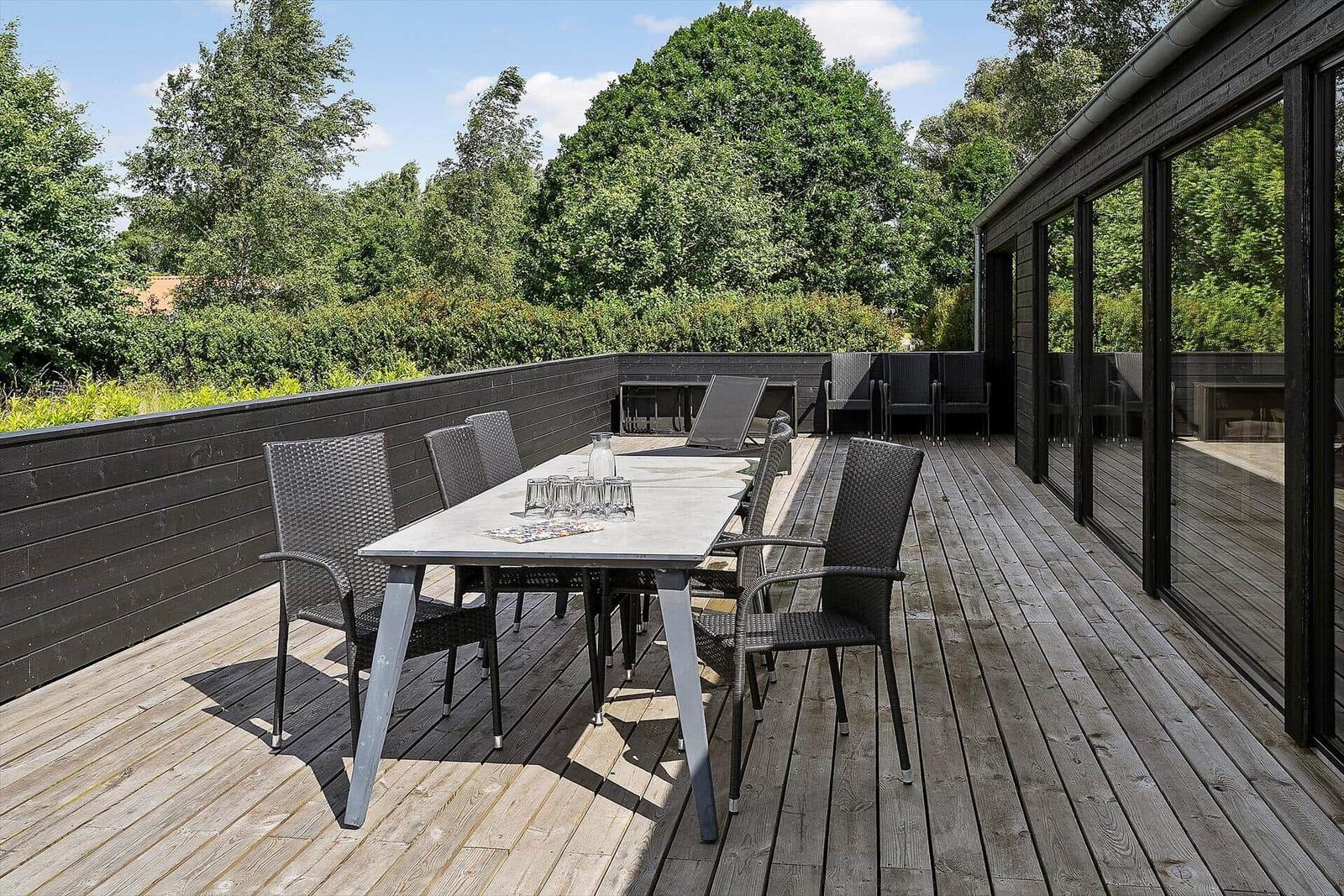 Wooden terrace with table and chairs, view of a modern wooden house in rural surroundings.