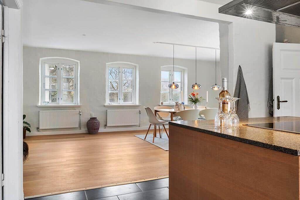 Kitchen with wooden countertop, white cabinets, and window. A board hangs on the wall.