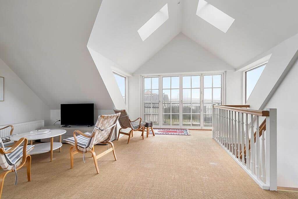 Living space with two chairs, sofa and table under sloped ceilings with skylights.