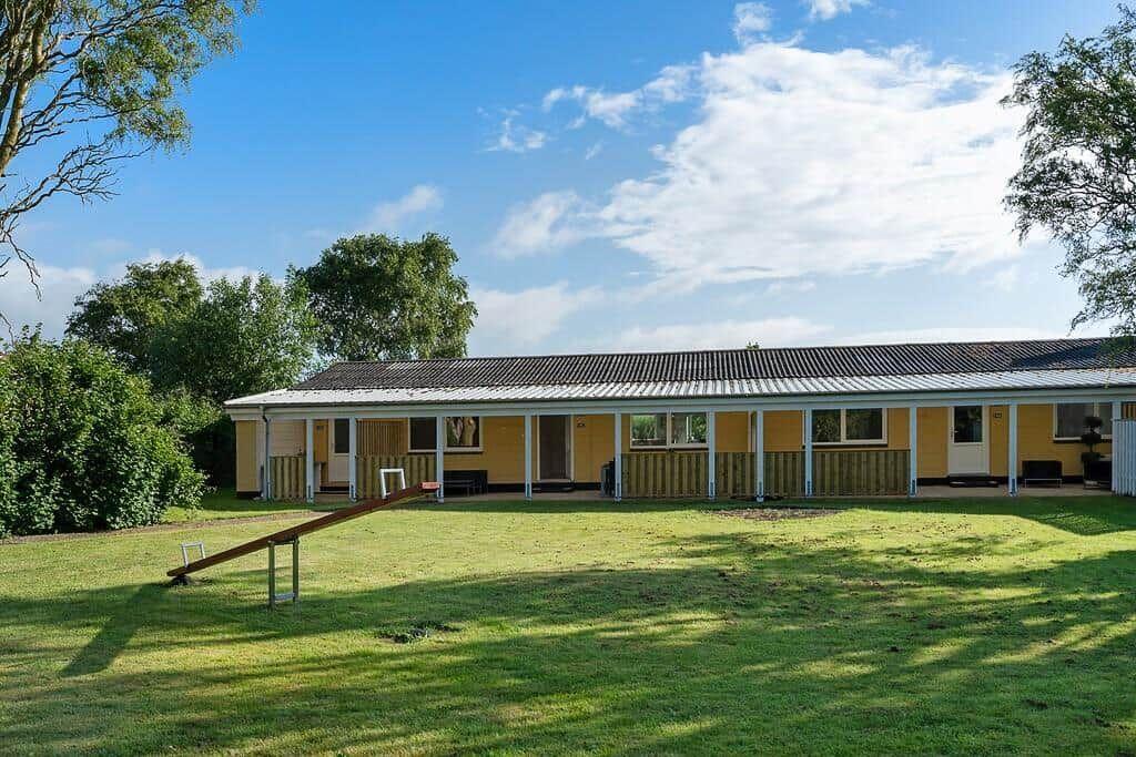 Ein gelbes Haus mit weißer Veranda und schwarzem Dach unter blauem Himmel.