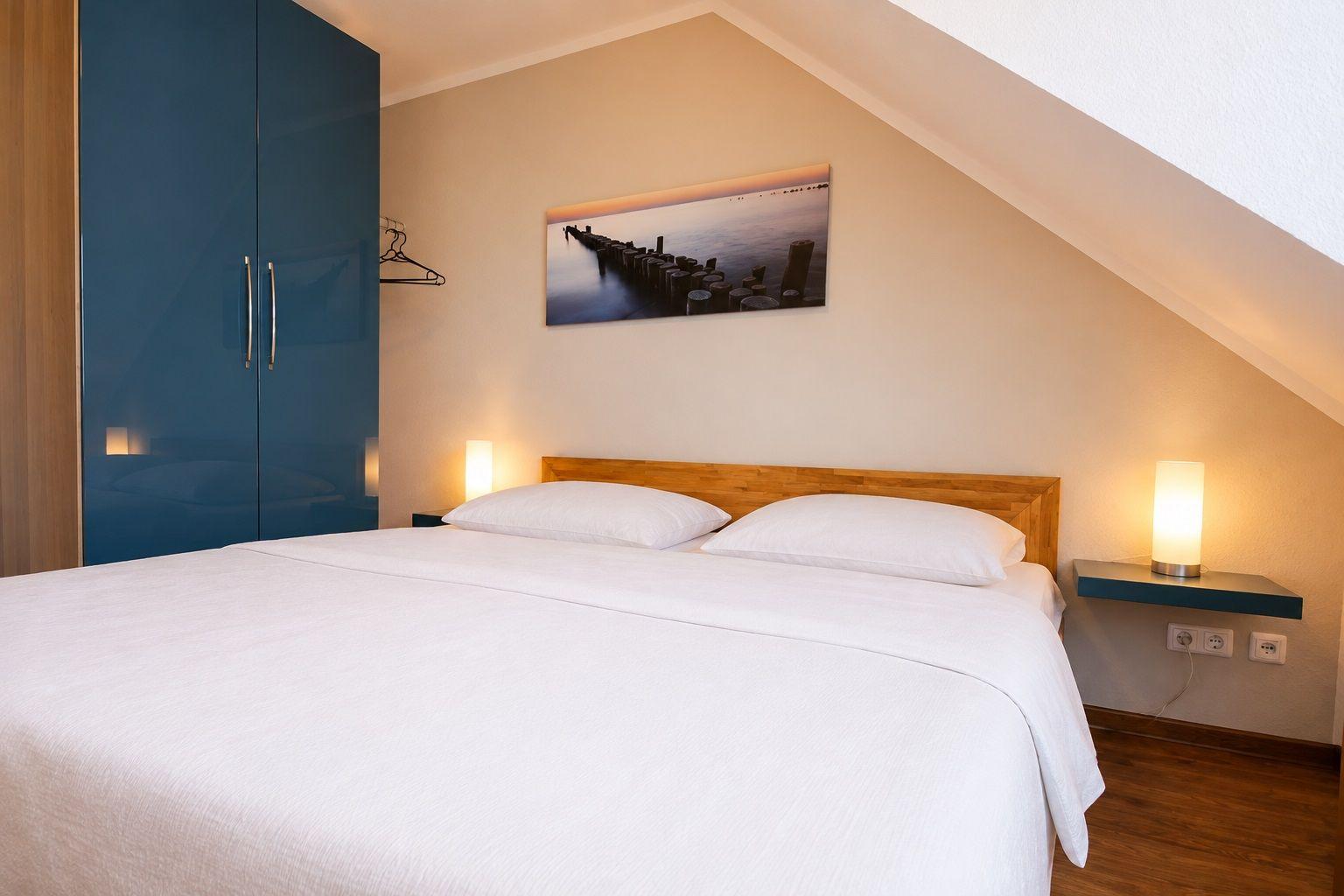 Schlafzimmer mit Doppelbett, blauem Schrank und Wandbild.