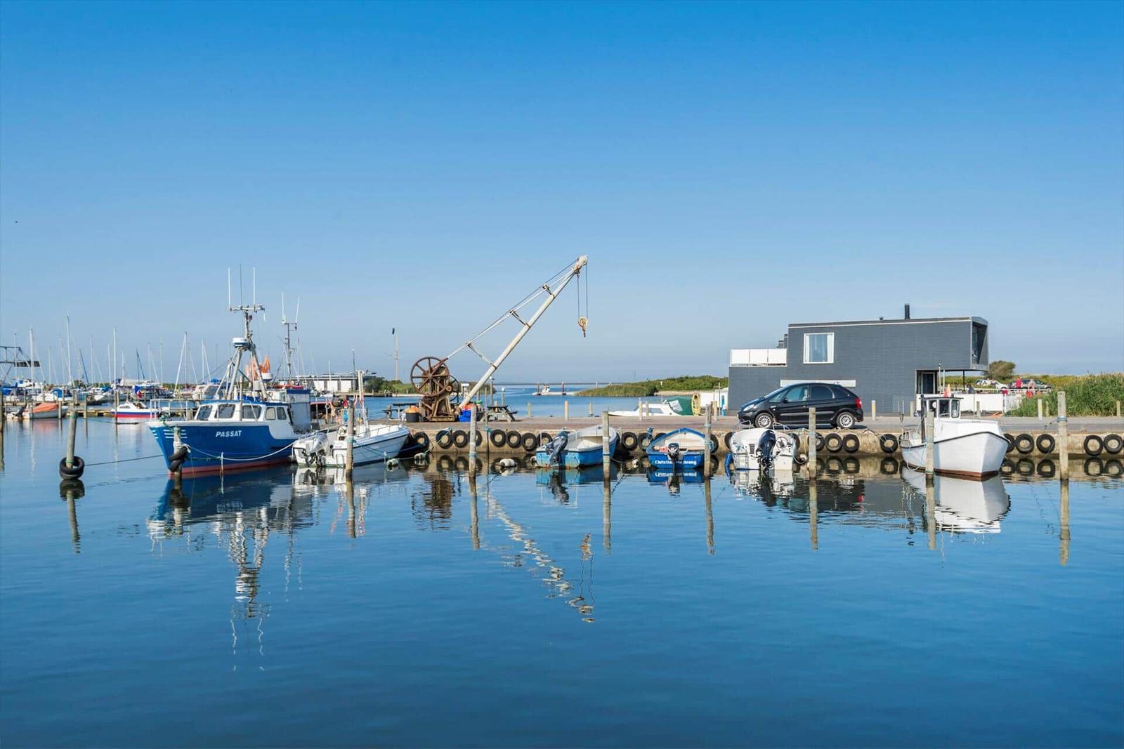 Gäste sitzen unter roten Sonnenschirmen am Hafen mit Booten im Hintergrund.