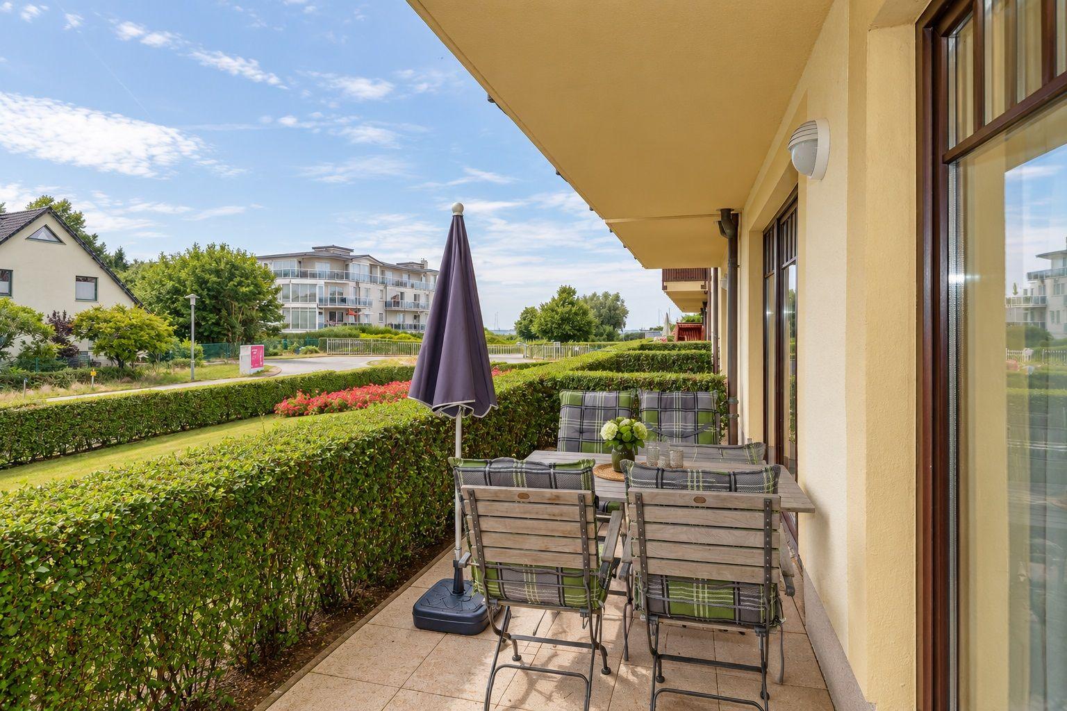 Terrasse mit Sitzgruppe, Sonnenschutz und Blick auf Grünanlagen und Wohngebäude.