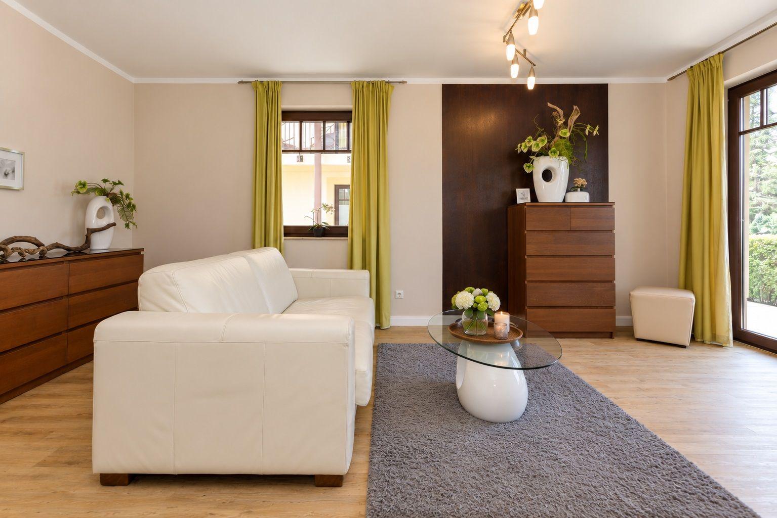 Wohnzimmer mit weißem Sofa, Holzmöbeln und grünen Vorhängen.