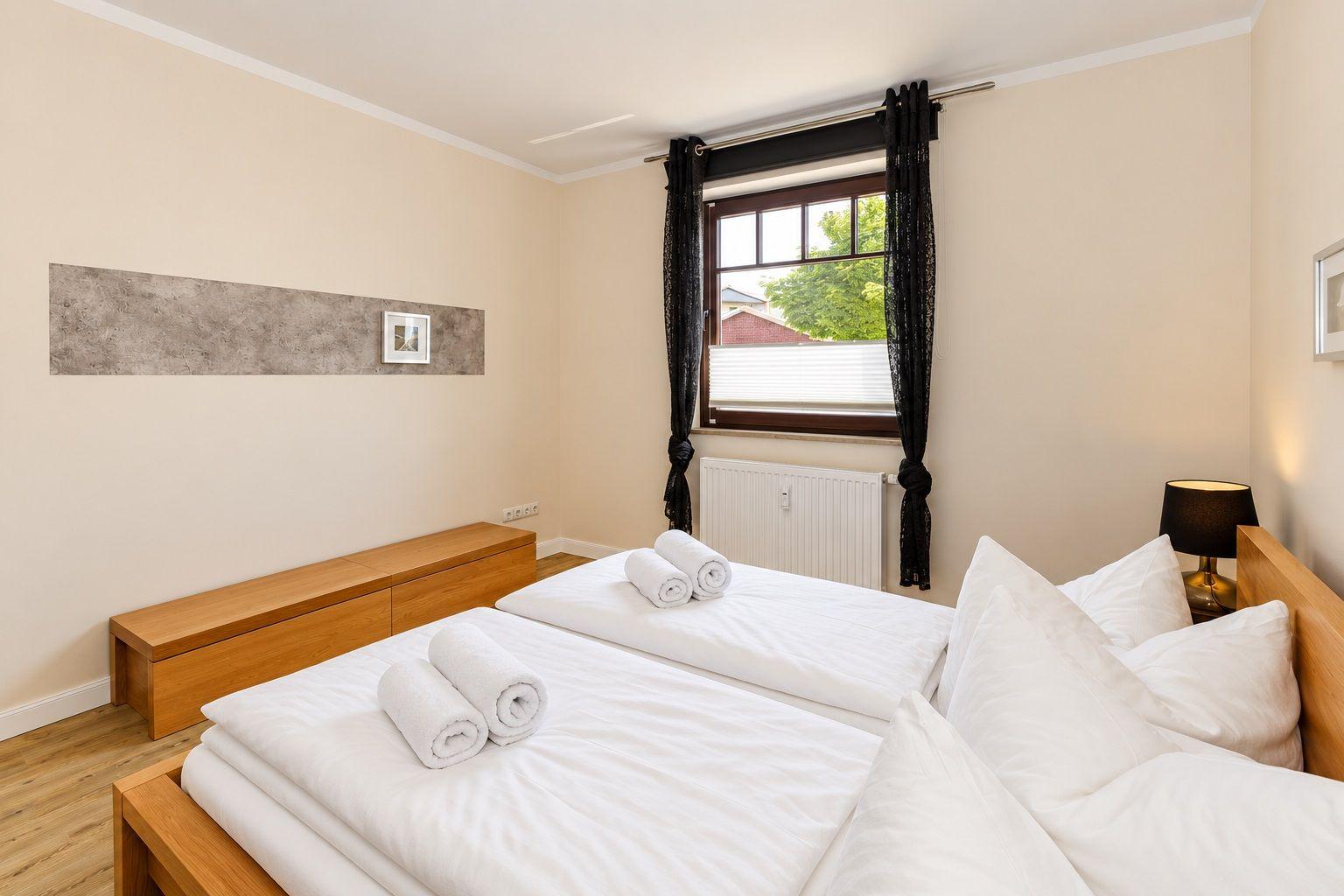 Schlafzimmer mit Doppelbett, Fenster und Holzmöbel.