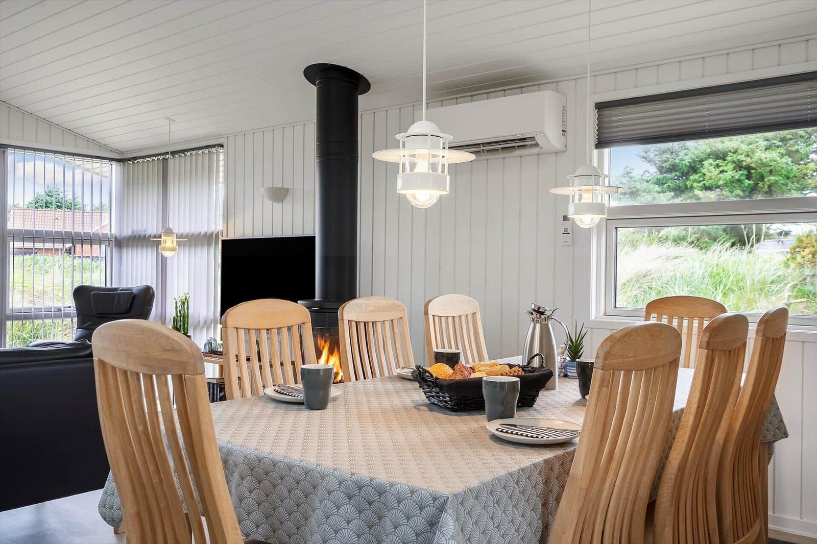 Wohnzimmer mit Sitzgelegenheiten, Kamin und TV. Große Fenster mit Blick auf Grünflächen.