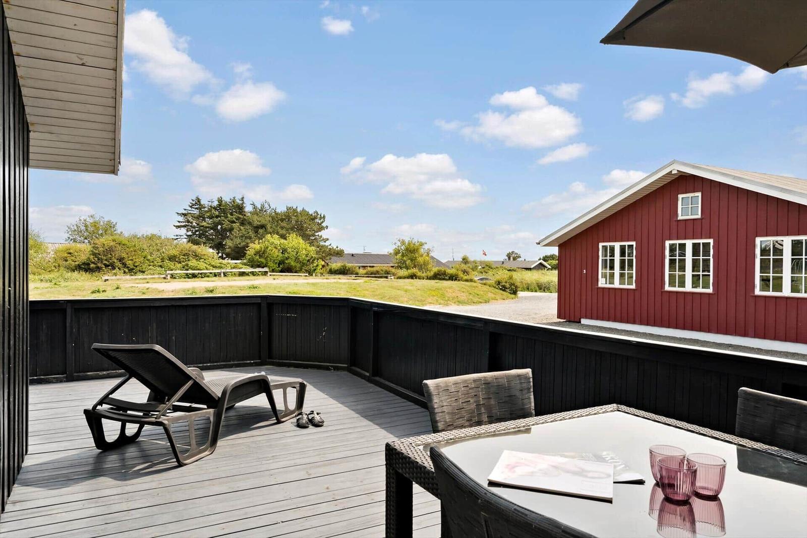 Terrasse mit Tisch, Stühlen und Sonnenschirm. Wetsuit hängt an der Tür.