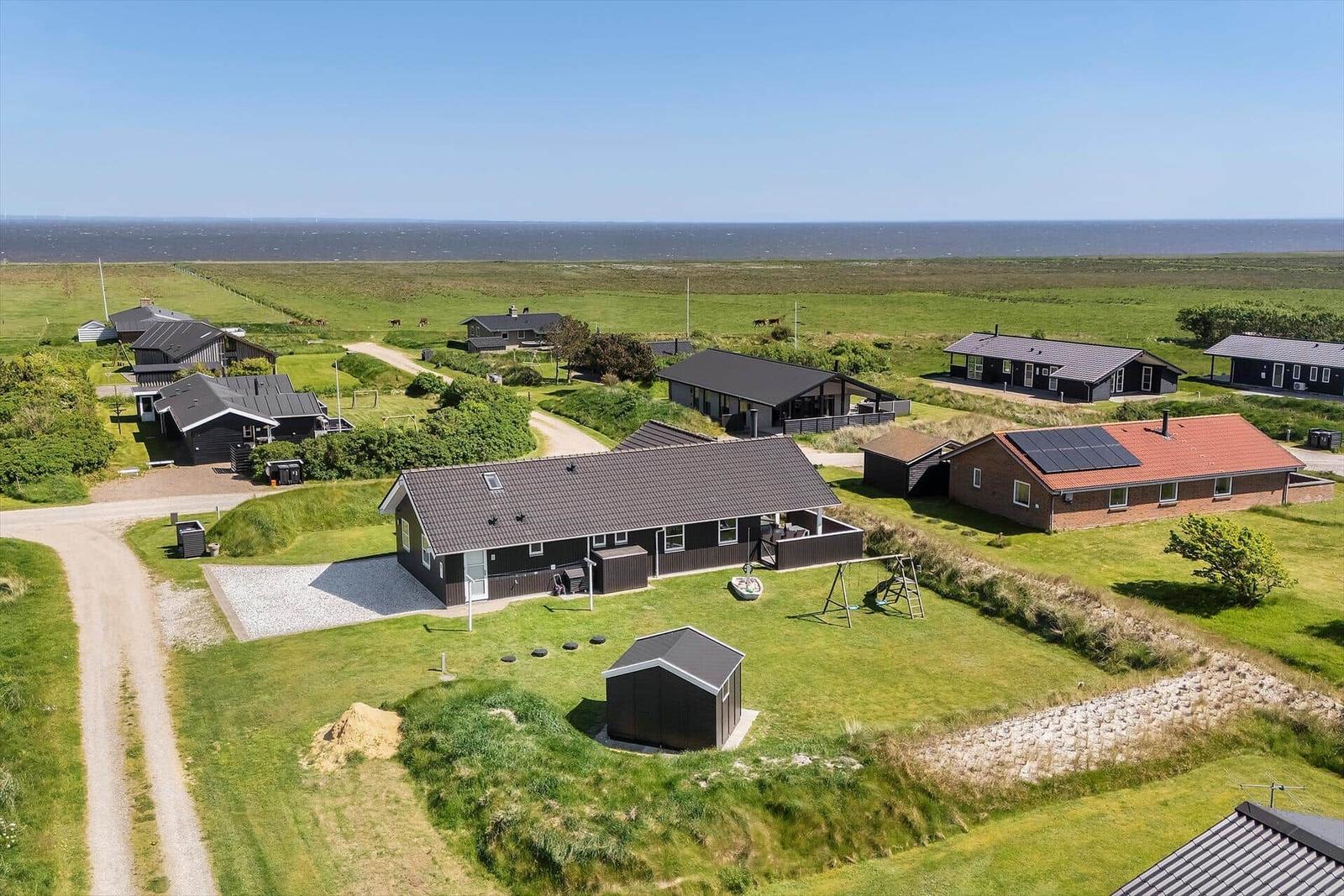 Weißer Leuchtturm auf grünen Dünen mit Blick auf das Meer.