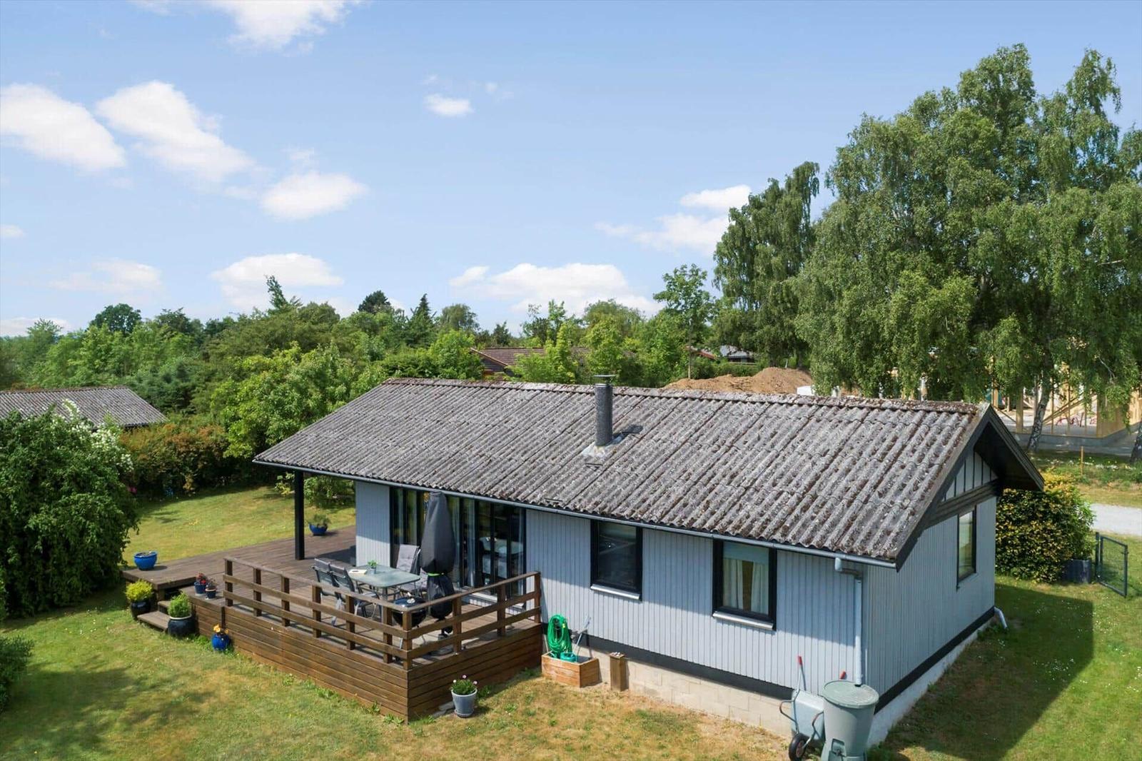 Ein Haus mit Terrasse, Garten und Blick auf Bäume.