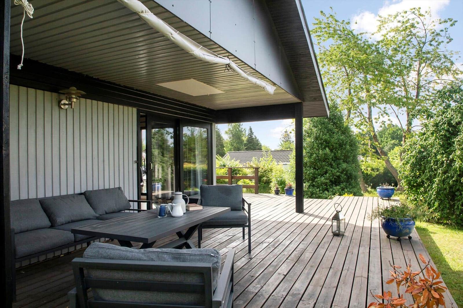Moderne Villa mit Terrasse, umgeben von grüner Vegetation und einem Rasen.