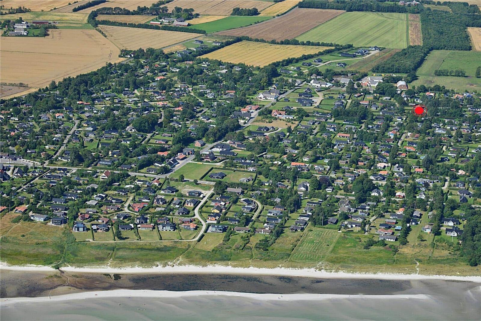 Luftbild eines Dorfes mit Häusern, Grünflächen und Strand. Ein roter Punkt markiert eine Position.