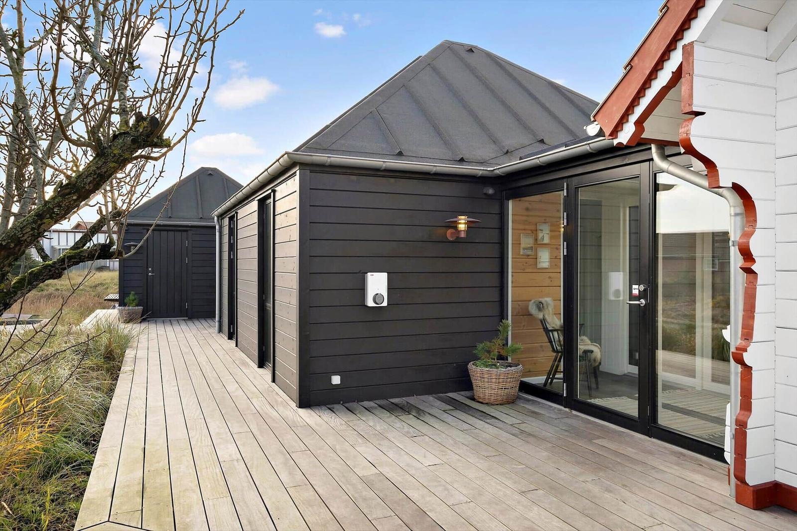 Black wooden cabin with deck, two lounge chairs, and outdoor wooden bathtub.