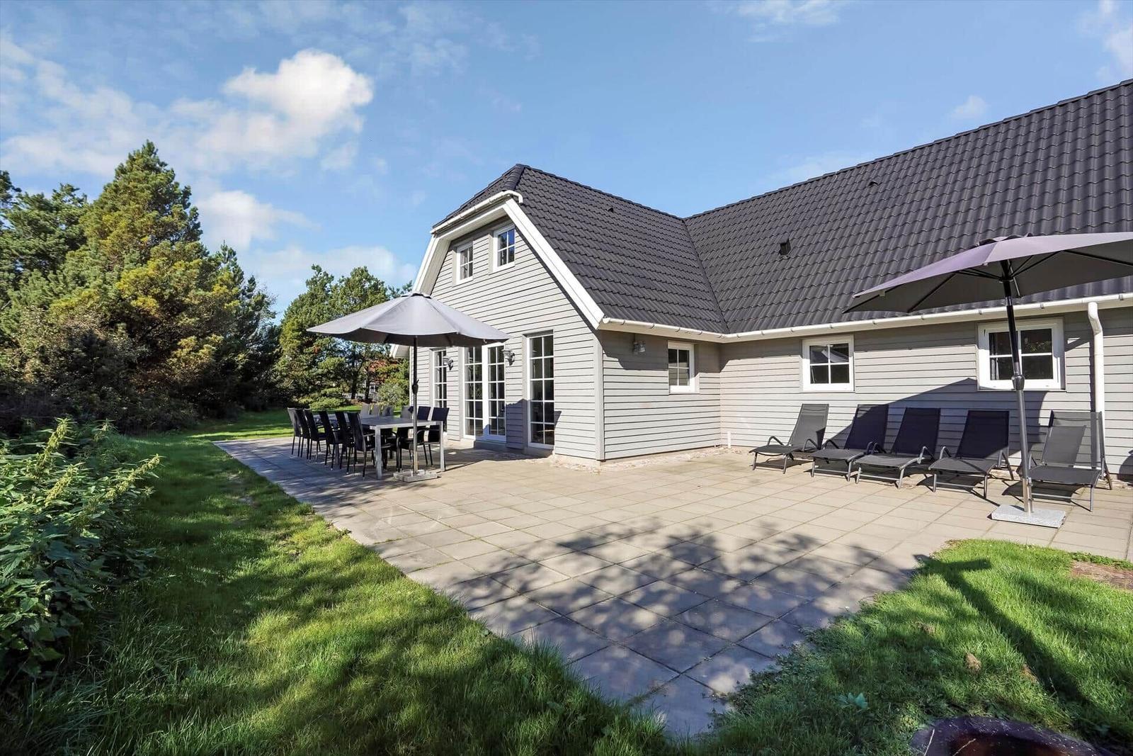 Ein Haus mit großem Garten, Fußballtor und Terrasse unter blauem Himmel.