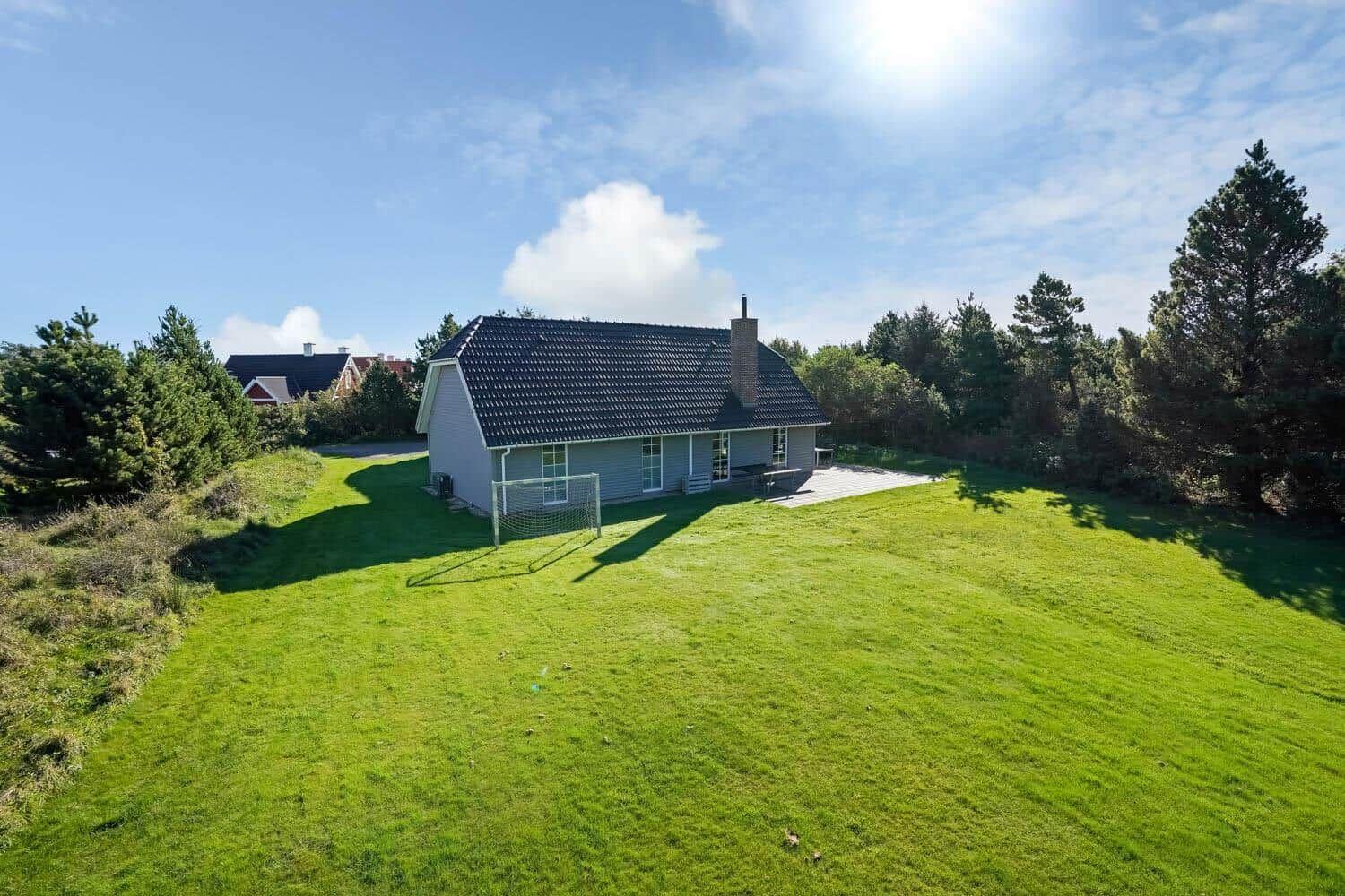 Ein Haus mit dunklem Dach und Terrasse auf grünem Grundstück mit Bäumen.