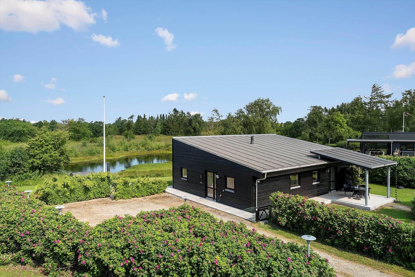 Modern wooden house with terrace, lounge chairs, and garden. Large windows and outdoor deck.