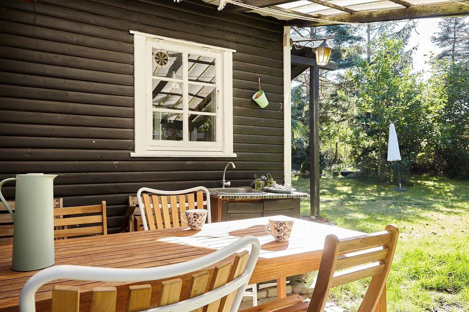 Room with wooden walls, windows, and chairs. Outside trees and sky.