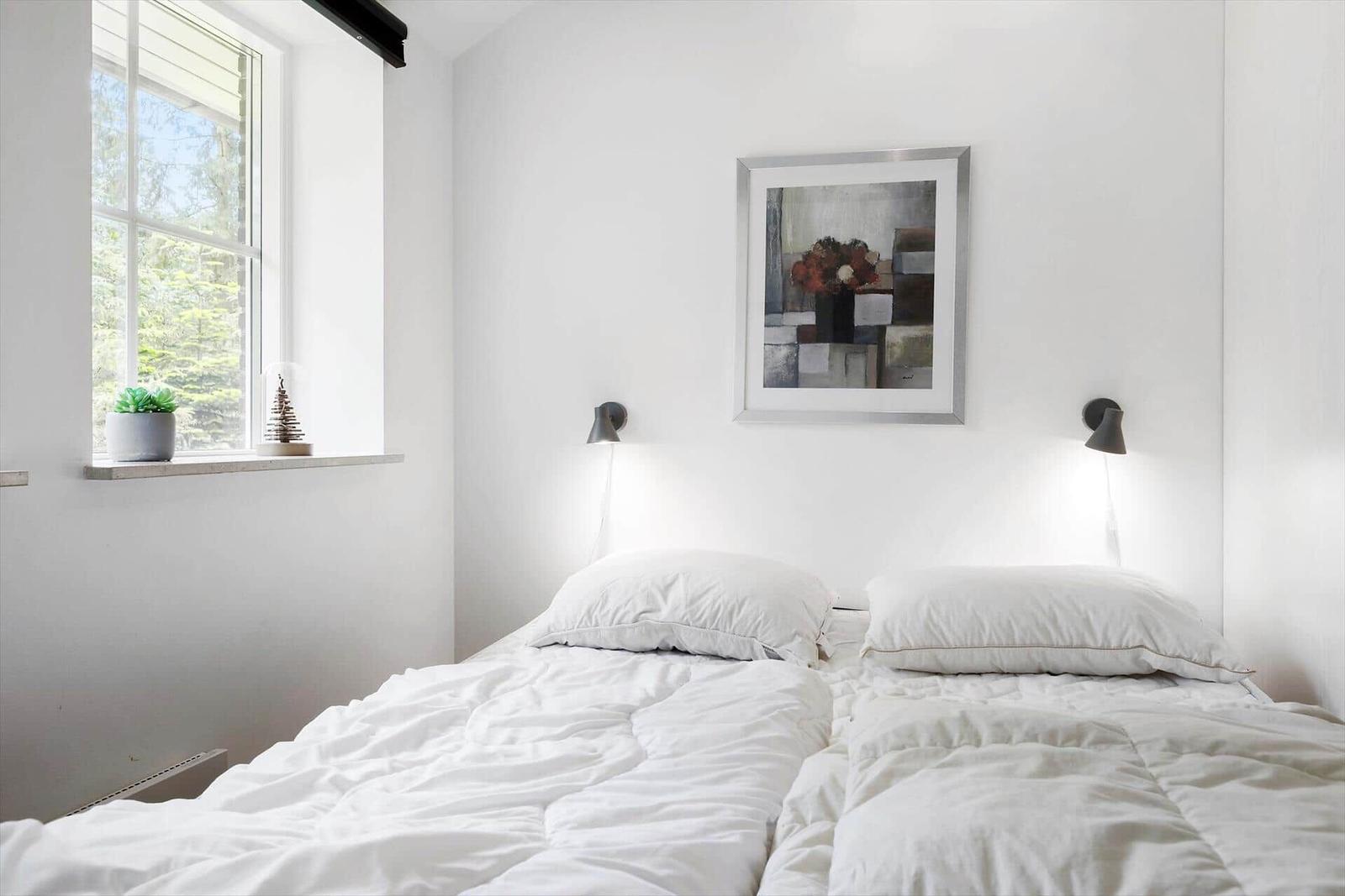 Two beds under a sloped ceiling with two triangular windows and wooden floor.