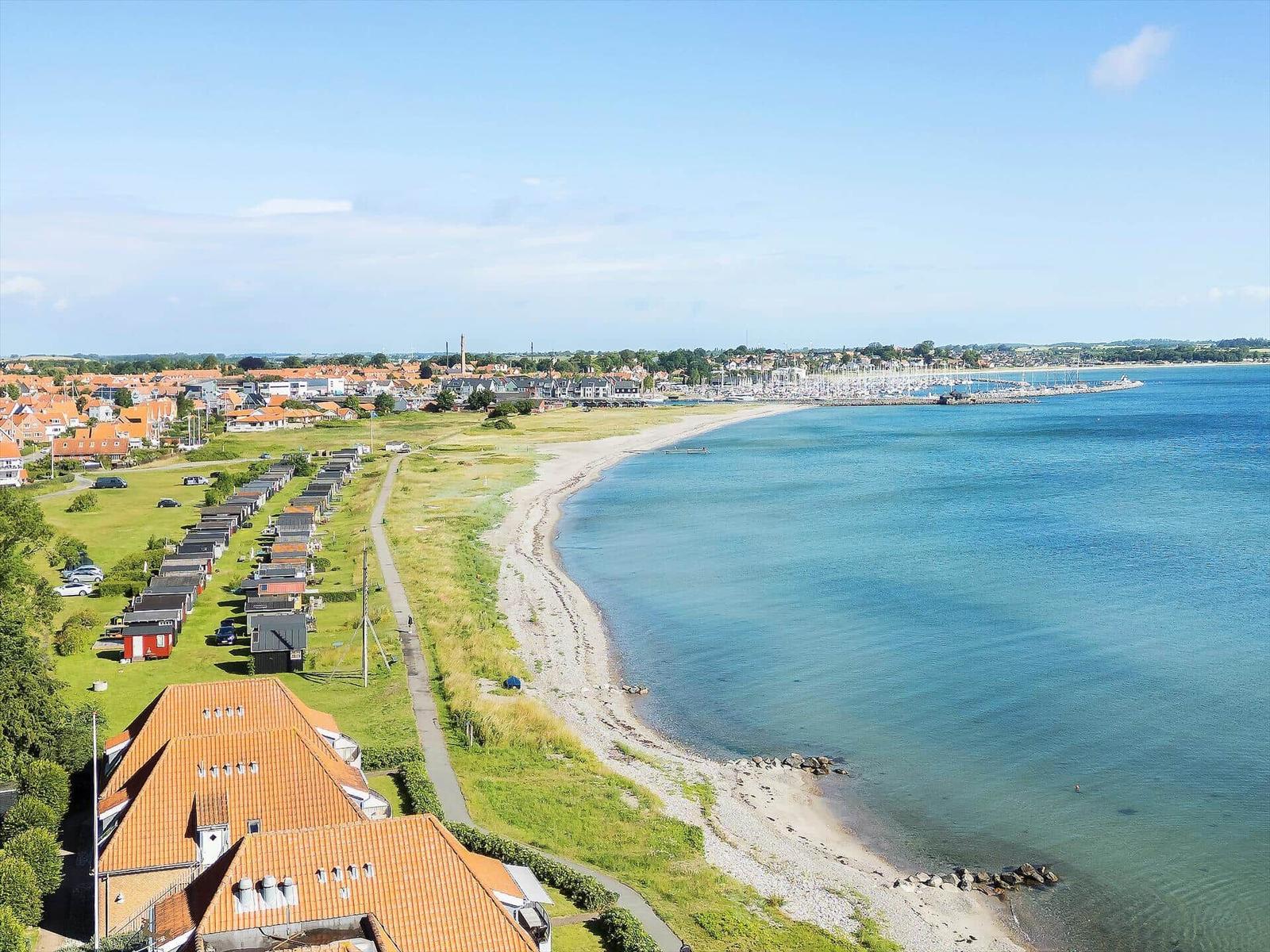 Aerial view of coastal town with red-roofed houses, greenery, and a calm sea.