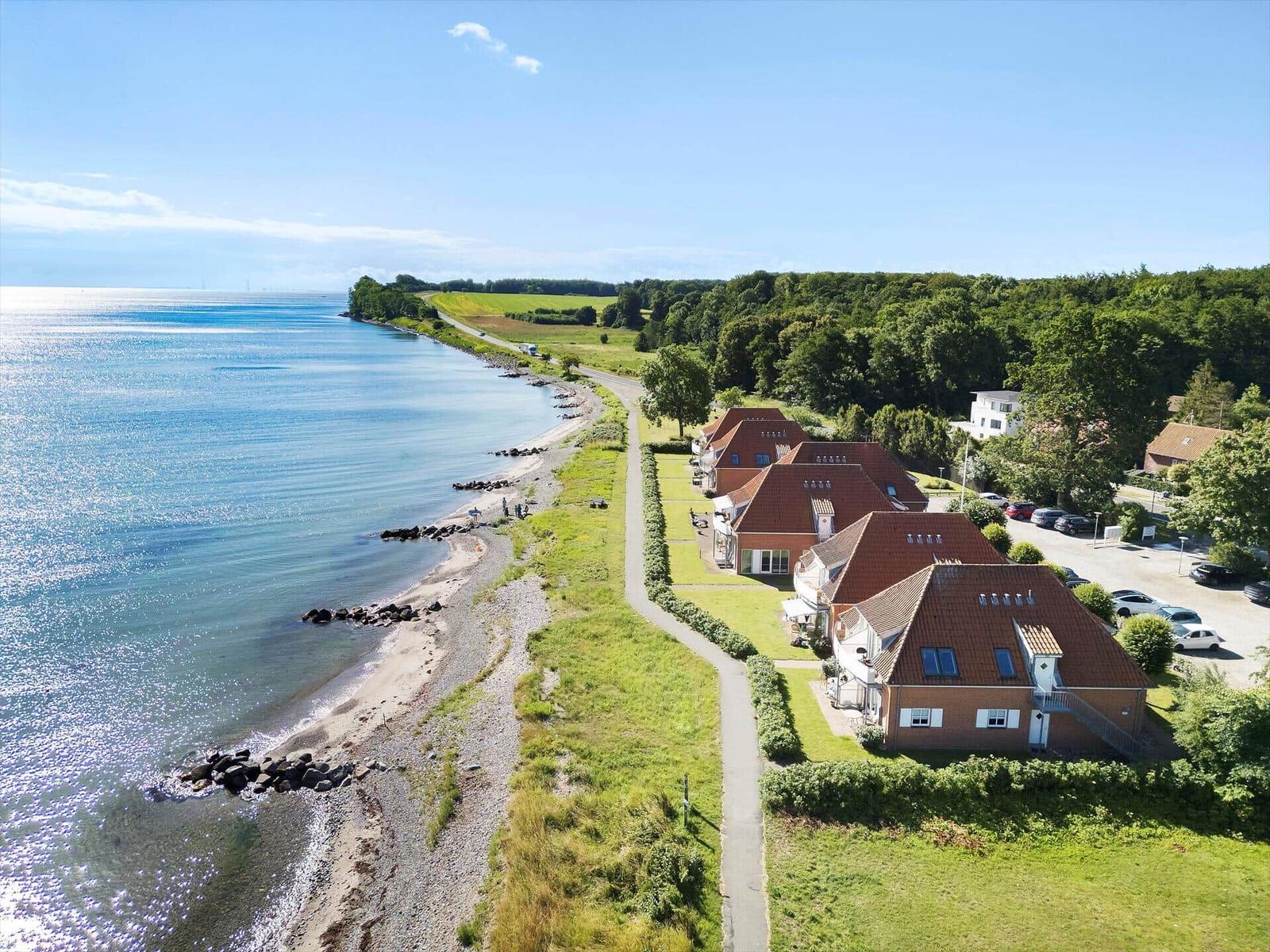 Aerial view of beachfront houses with red roofs and parking area near shoreline.