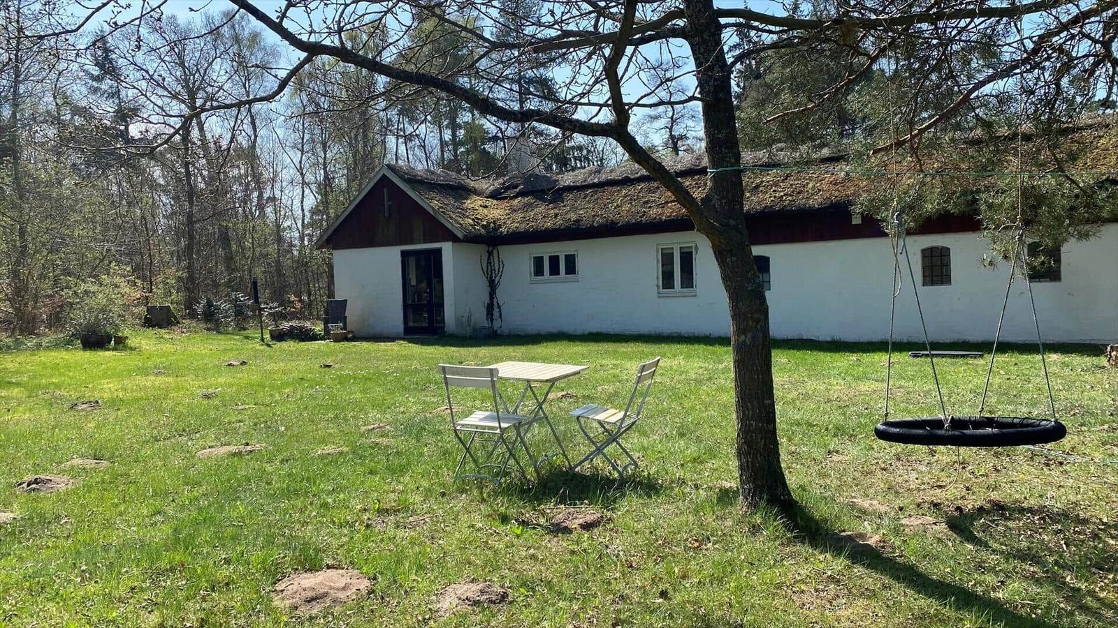 Außenbereich mit Tisch, Stühlen und Pflanzen vor einer Hauswand mit Glastür.