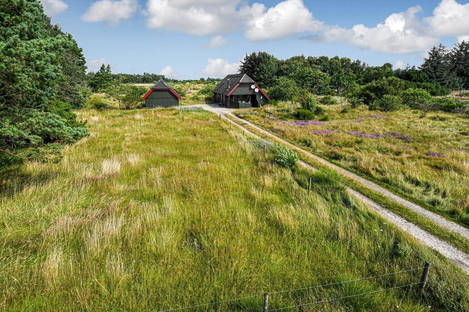 Haus mit Strohdach steht auf grünem Grundstück neben Wasser. Zwei Autos parken auf dem Weg.