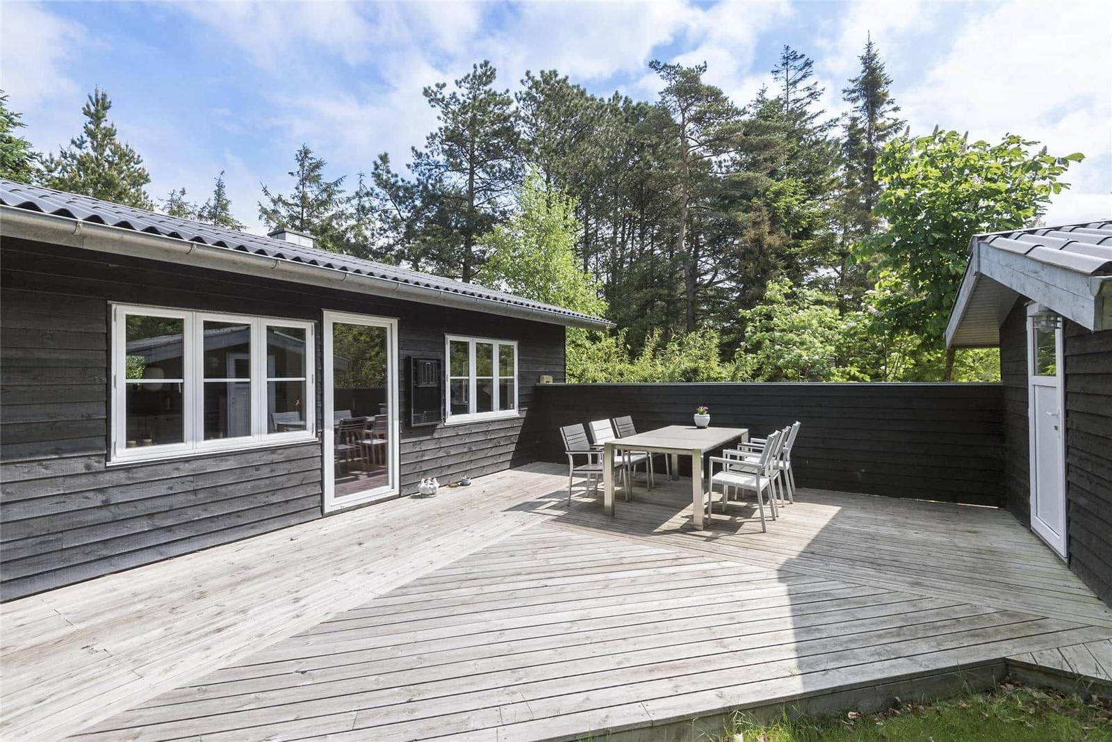 Ein schwarzes Holzhaus mit Terrasse und Garten. Umgeben von Bäumen und Gras.