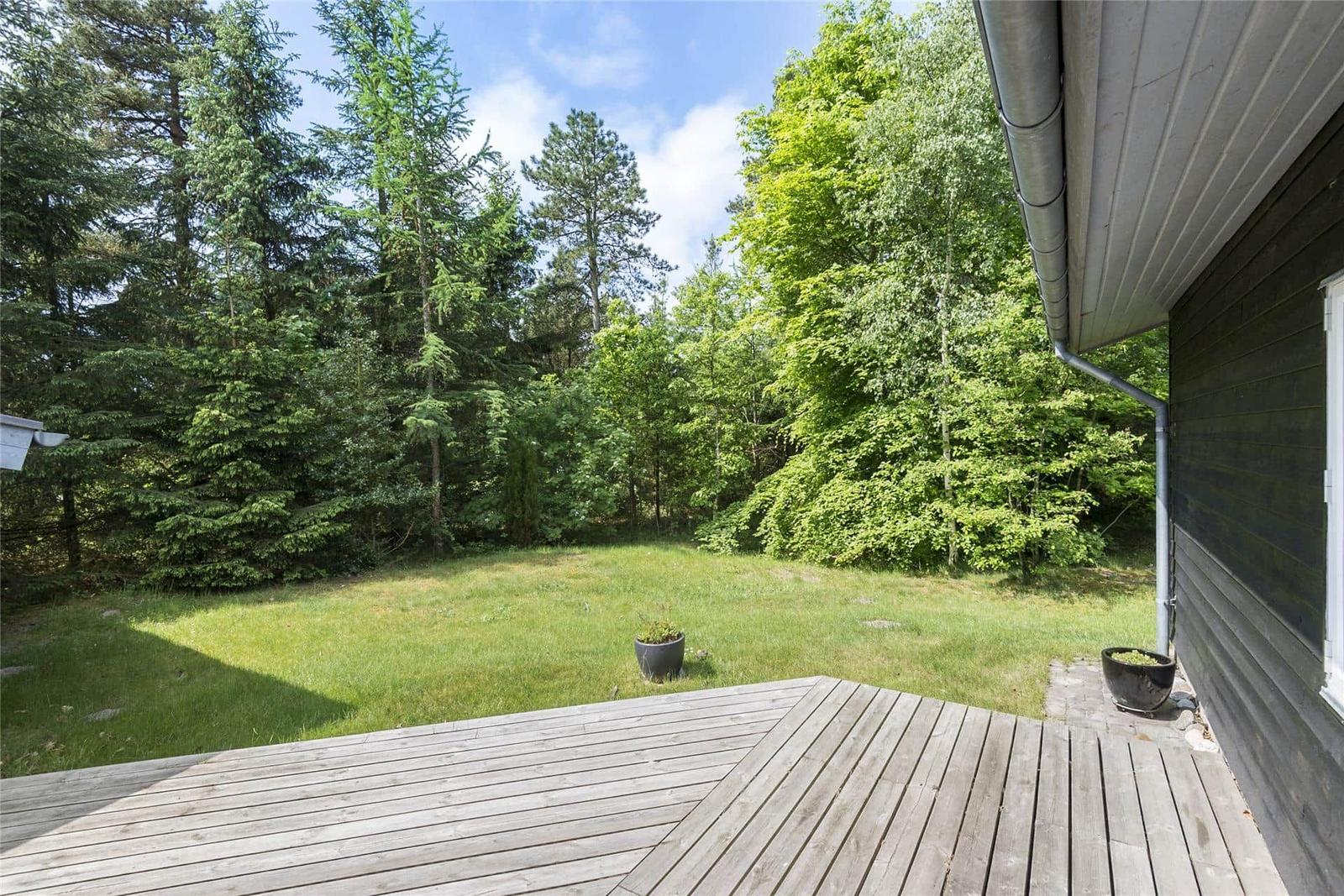 Terrasse mit Tisch und zwei Stühlen, umgeben von dunklem Holzzaun und grüner Vegetation.